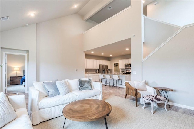 living area with baseboards, visible vents, and high vaulted ceiling