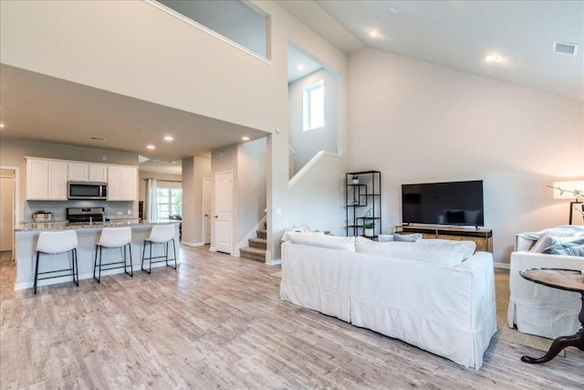 living area with light wood-style floors, stairs, visible vents, and high vaulted ceiling