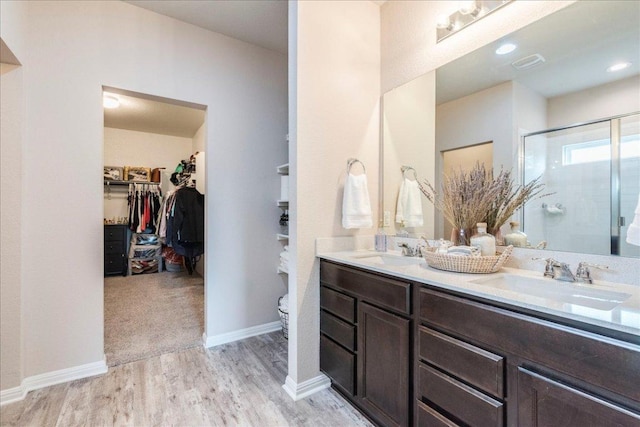 bathroom featuring wood finished floors, a shower stall, a spacious closet, and a sink