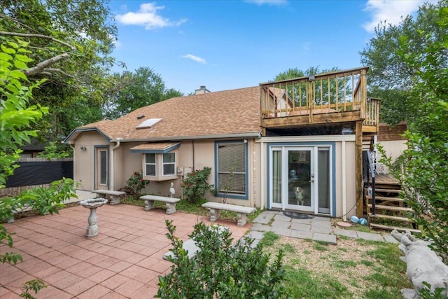 rear view of house with a chimney, a wooden deck, roof with shingles, a patio area, and stairs