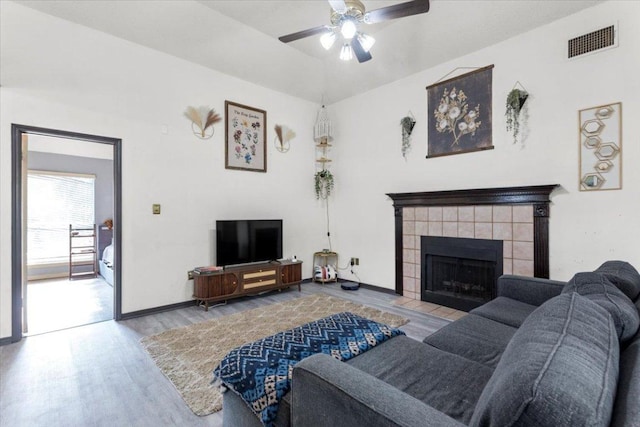 living room with a fireplace, a ceiling fan, visible vents, baseboards, and wood finished floors