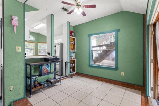 interior space featuring light tile patterned floors, a ceiling fan, visible vents, a textured wall, and lofted ceiling