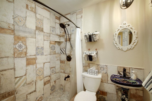 bathroom with toilet, a tile shower, tile walls, and a sink