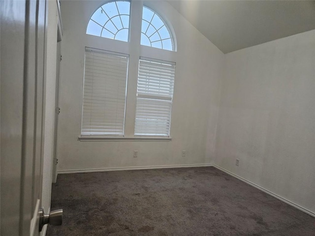 spare room featuring lofted ceiling, dark colored carpet, and baseboards