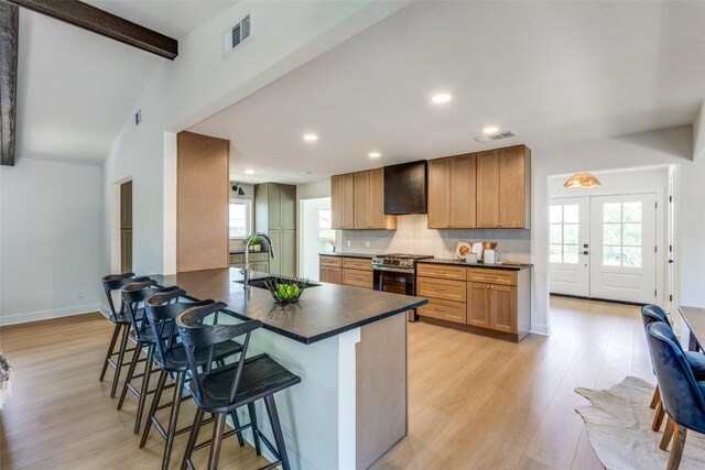 kitchen with stainless steel gas stove, dark countertops, a kitchen bar, a sink, and visible vents