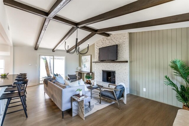 living room with an inviting chandelier, lofted ceiling with beams, a brick fireplace, baseboards, and wood finished floors
