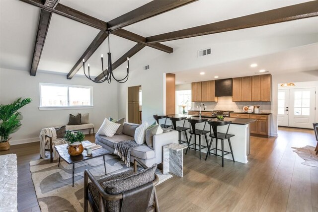 living area featuring visible vents, lofted ceiling with beams, plenty of natural light, and light wood finished floors