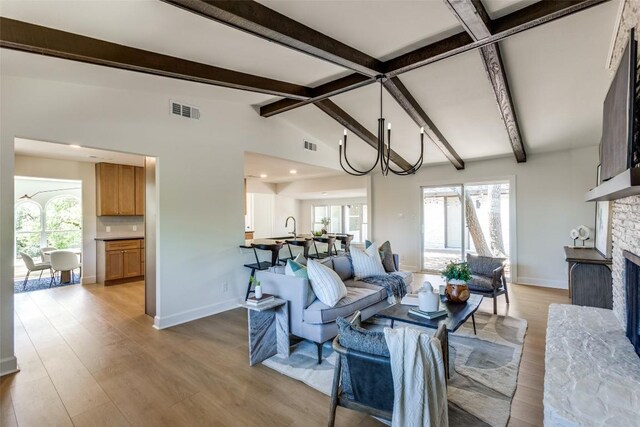 living room with vaulted ceiling with beams, visible vents, light wood-style flooring, and a stone fireplace