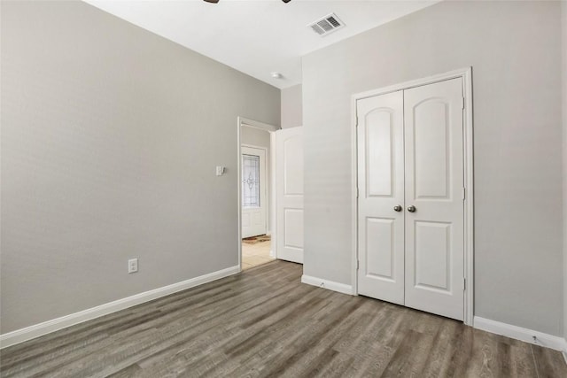 unfurnished bedroom with a closet, visible vents, wood finished floors, and baseboards