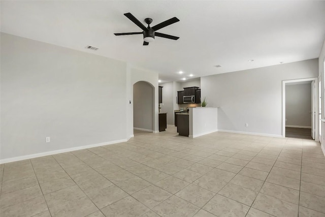 unfurnished living room featuring light tile patterned floors, ceiling fan, visible vents, baseboards, and arched walkways