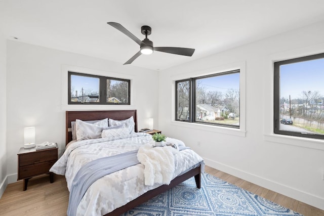 bedroom featuring baseboards, light wood finished floors, and multiple windows