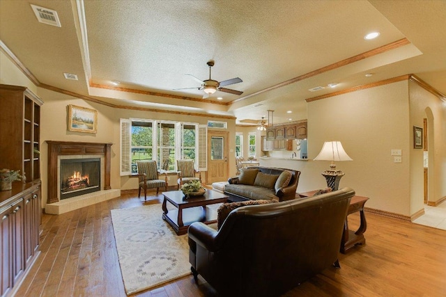 living area featuring crown molding, ceiling fan, a premium fireplace, and a raised ceiling