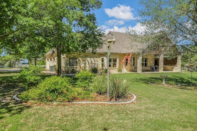 rear view of property with a yard, a patio, and stone siding