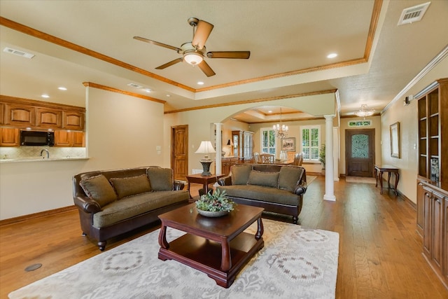 living room featuring a tray ceiling, crown molding, visible vents, ornate columns, and arched walkways