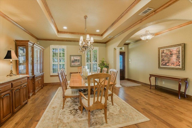 dining space with visible vents, arched walkways, a chandelier, light wood-type flooring, and a raised ceiling
