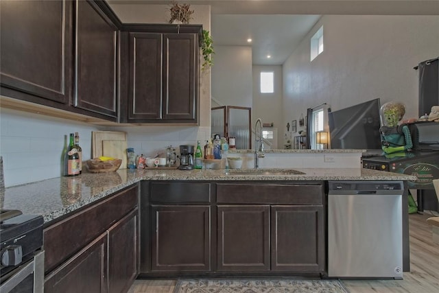 kitchen featuring dark brown cabinetry, stainless steel dishwasher, decorative backsplash, a sink, and a peninsula