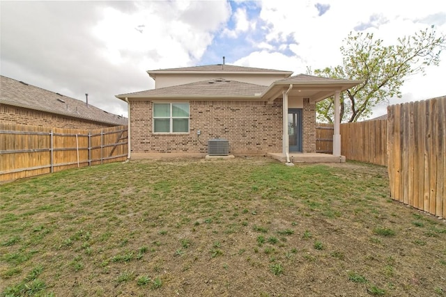 back of property featuring a shingled roof, central AC unit, a fenced backyard, a lawn, and brick siding