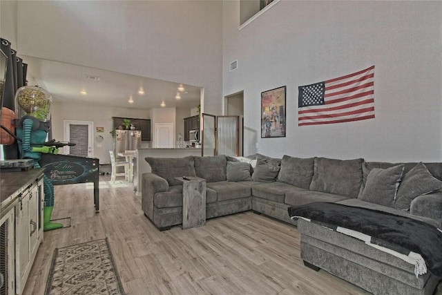 living area with visible vents, light wood finished floors, and a towering ceiling