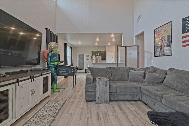 living area featuring visible vents, light wood-style floors, and a towering ceiling