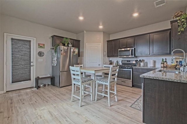 kitchen featuring a sink, stainless steel appliances, light wood-style floors, dark brown cabinetry, and visible vents