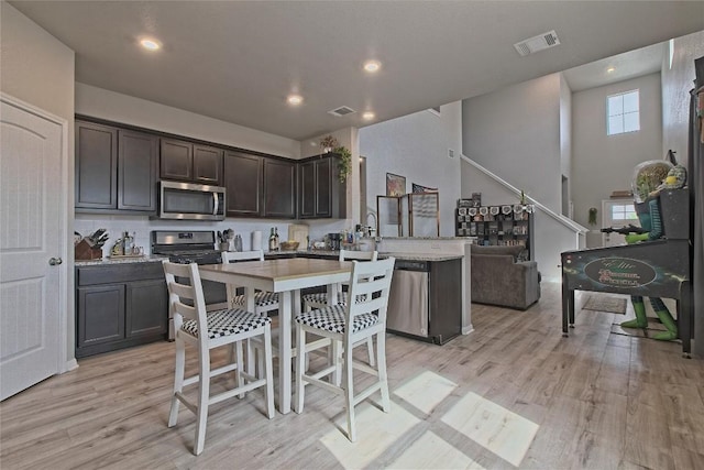 kitchen with dark brown cabinetry, visible vents, light wood-style flooring, a peninsula, and appliances with stainless steel finishes