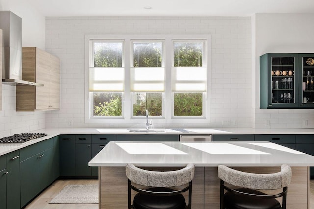 kitchen with a breakfast bar, wall chimney range hood, light countertops, and stainless steel gas stovetop