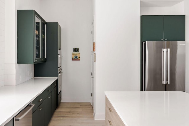 kitchen with decorative backsplash, light wood-style floors, stainless steel appliances, green cabinets, and light countertops