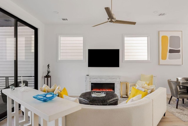 living area featuring wood finished floors, ceiling fan, visible vents, and a high end fireplace