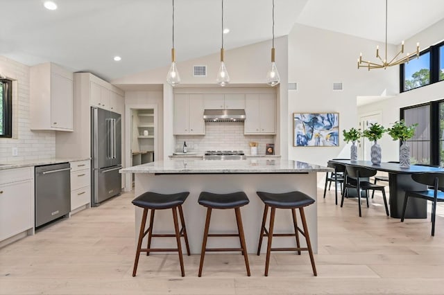 2001 Circle Hvn, Austin, TX 78741 - kitchen featuring stainless steel appliances, under cabinet range hood, backsplash, a breakfast bar area, and light wood-style flooring