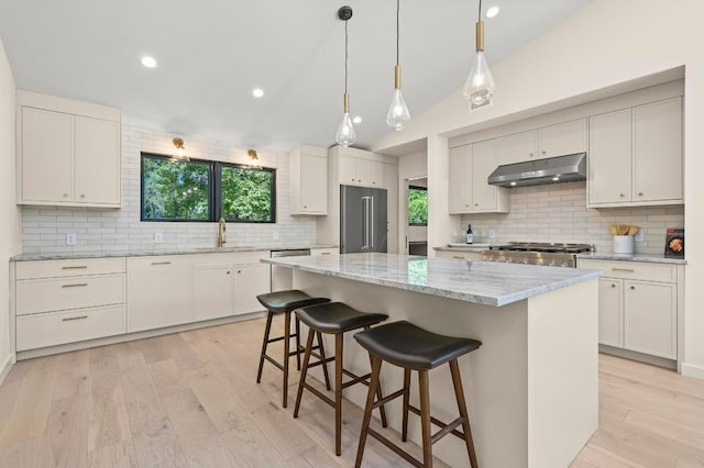 2001 Circle Hvn, Austin, TX 78741 - kitchen featuring under cabinet range hood, high end fridge, decorative backsplash, a kitchen breakfast bar, and lofted ceiling