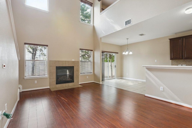 unfurnished living room featuring hardwood / wood-style flooring, visible vents, an inviting chandelier, a tiled fireplace, and a high ceiling