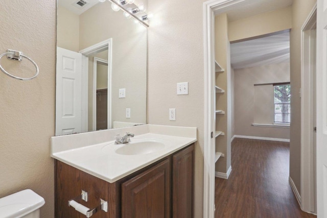 bathroom featuring wood finished floors, toilet, vanity, baseboards, and visible vents