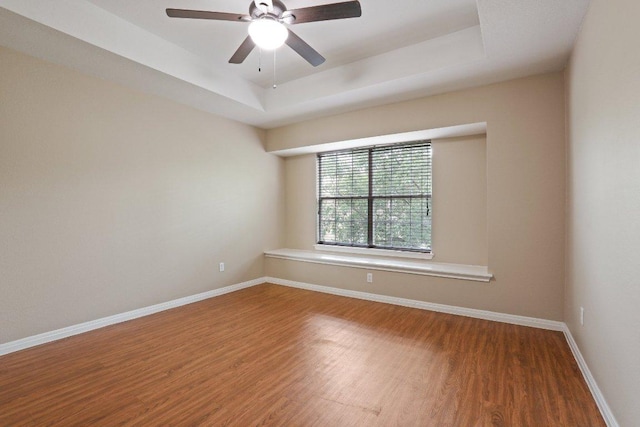 spare room with ceiling fan, baseboards, wood finished floors, and a tray ceiling