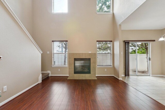 unfurnished living room with a towering ceiling, a healthy amount of sunlight, hardwood / wood-style floors, and a tile fireplace