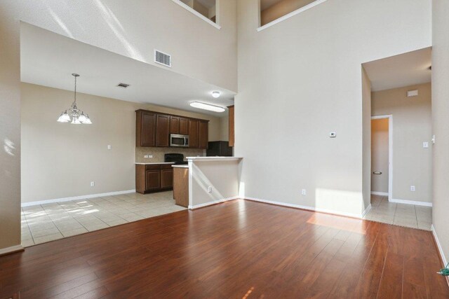 unfurnished living room featuring an inviting chandelier, visible vents, light wood-style flooring, and baseboards