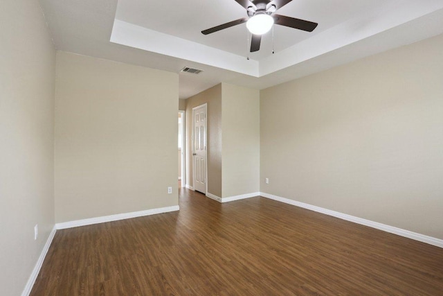 empty room featuring a raised ceiling, ceiling fan, visible vents, dark wood-style floors, and baseboards