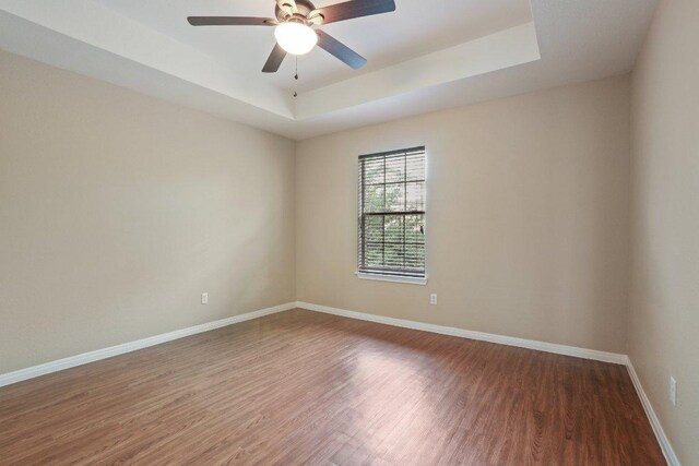 unfurnished room with baseboards, wood finished floors, ceiling fan, and a tray ceiling