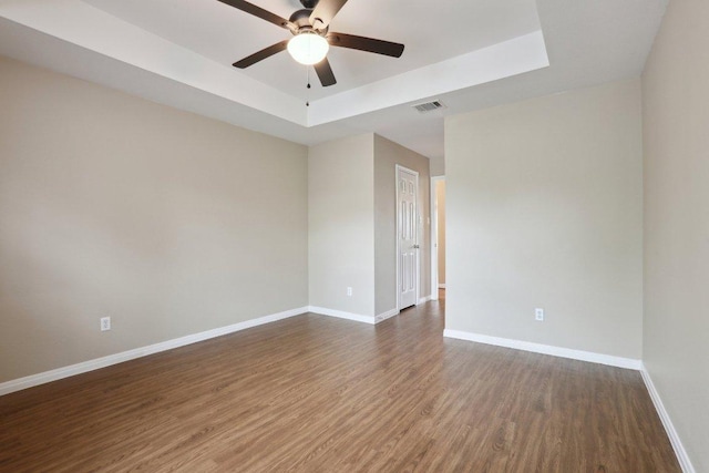 spare room with wood finished floors, a raised ceiling, a ceiling fan, and baseboards