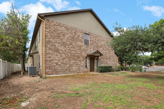 view of front facade with brick siding, fence, and cooling unit