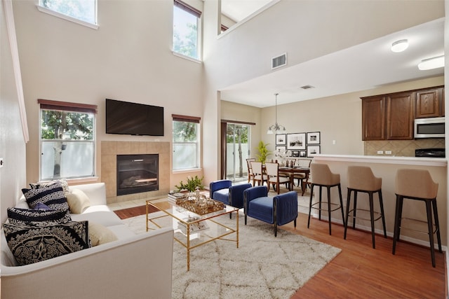 living room featuring visible vents, wood finished floors, a tile fireplace, and a high ceiling