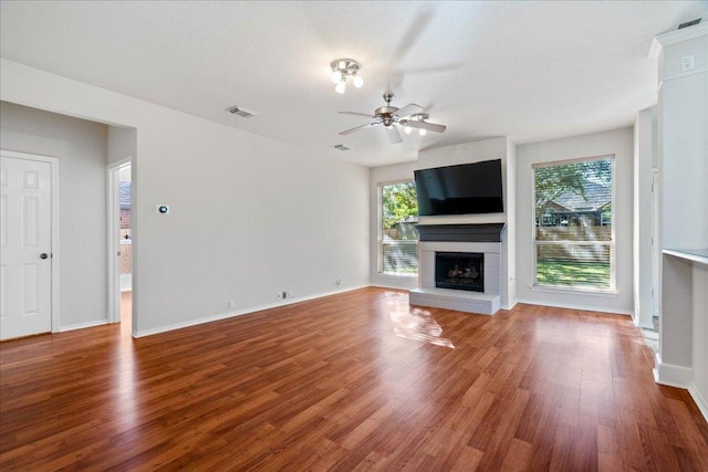 unfurnished living room featuring plenty of natural light, ceiling fan, wood finished floors, and a fireplace