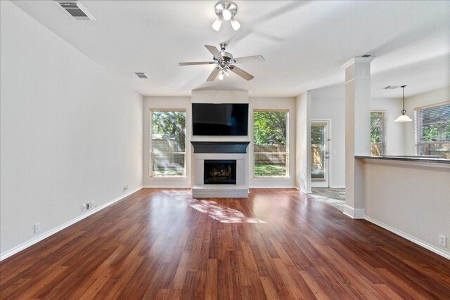 unfurnished living room featuring a wealth of natural light, visible vents, wood finished floors, and a brick fireplace
