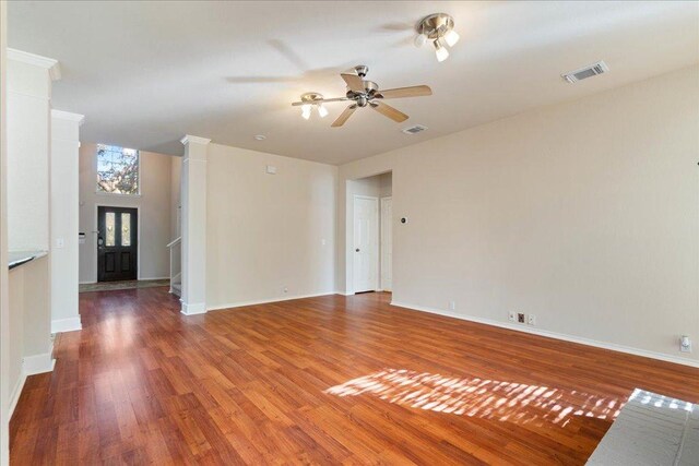 unfurnished living room with wood finished floors, a ceiling fan, visible vents, and decorative columns