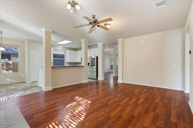 unfurnished living room featuring visible vents, ceiling fan, dark wood finished floors, and decorative columns