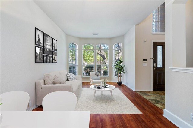 living room with dark wood-style floors, visible vents, and baseboards