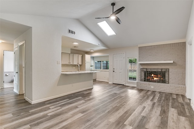 unfurnished living room with a brick fireplace, a ceiling fan, visible vents, baseboards, and wood finished floors