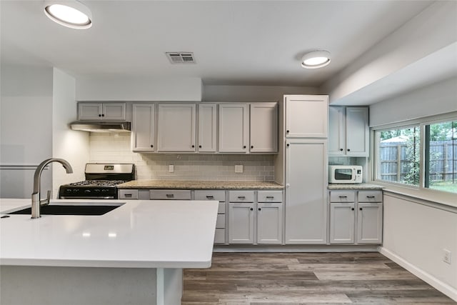 kitchen featuring a sink, light countertops, under cabinet range hood, stainless steel range with gas stovetop, and white microwave