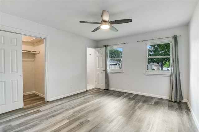 unfurnished bedroom with a walk in closet, baseboards, wood finished floors, and attic access