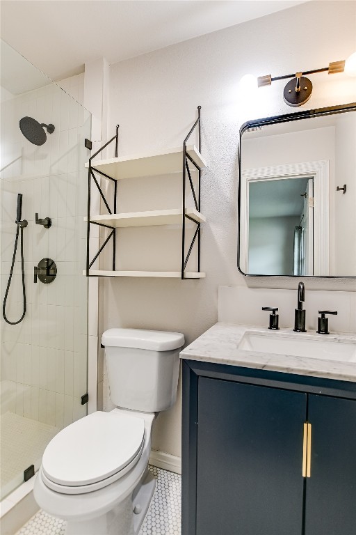 bathroom featuring tile patterned floors, a tile shower, toilet, and vanity