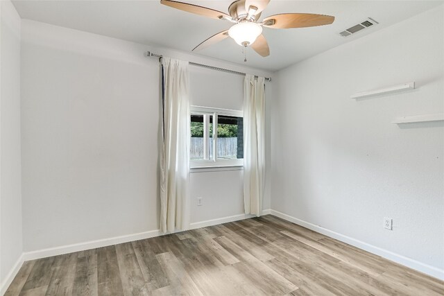 spare room featuring wood finished floors, visible vents, ceiling fan, and baseboards